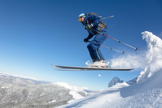 Ski skieur et saut en descente en haute montagne contre le ciel bleu