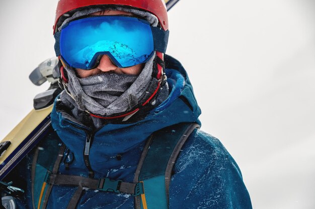 Skier équipé tenant des skis sur son épaule et regardant directement à la caméra portrait homme avec