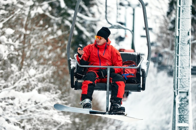 Skieur assis au téléski parlant au téléphone en haute montagne pendant la journée ensoleillée. Sports et loisirs d'hiver, loisirs de plein air.