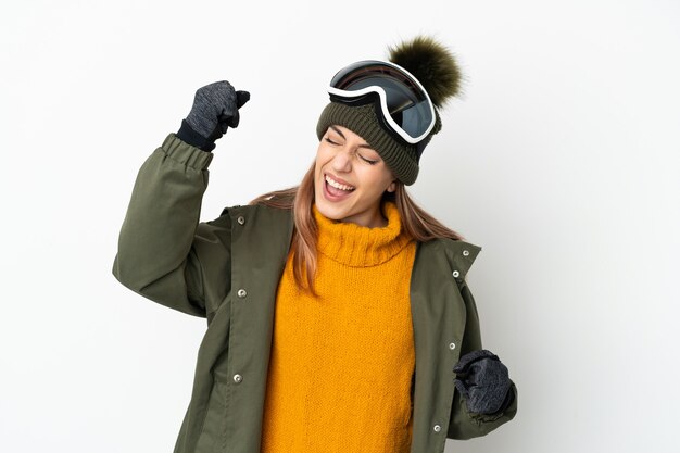 Skieur caucasien femme avec des lunettes de snowboard isolé sur un mur blanc célébrant une victoire