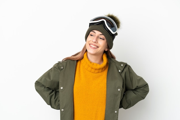 Skieur caucasien femme avec des lunettes de snowboard isolé sur un mur blanc posant avec les bras à la hanche et souriant