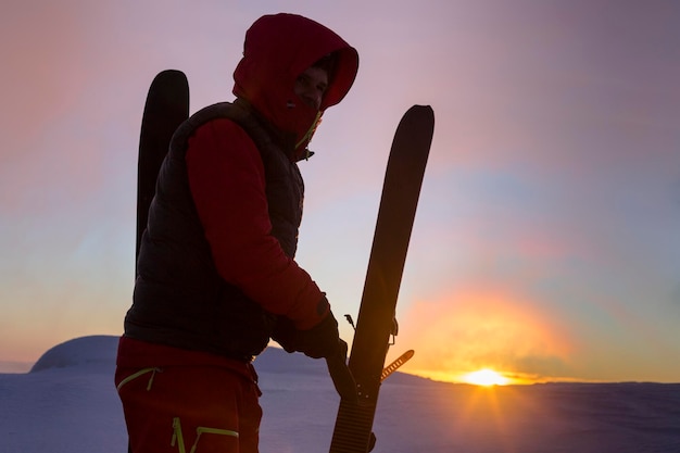 Le skieur enlève les peaux des skis sur le fond du lever du soleil orange du disque solaire dans les montagnes enneigées