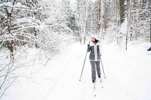 Skieur une femme dans une veste à membrane avec des bâtons de ski dans ses mains avec son dos sur le fond d'une forêt enneigée Ski de fond dans la forêt d'hiver sports de plein air mode de vie sain