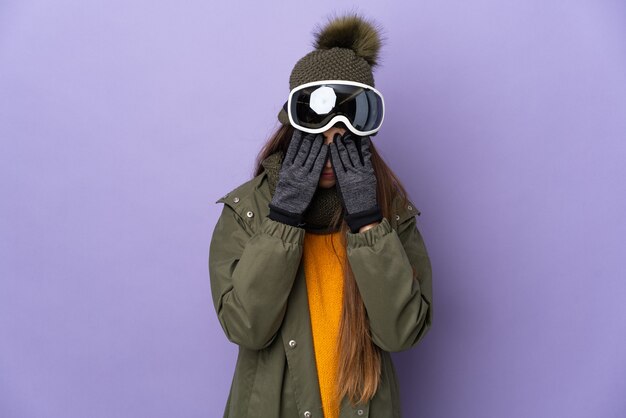 Skieur femme avec des lunettes de snowboard isolé sur un mur violet avec une expression fatiguée et malade