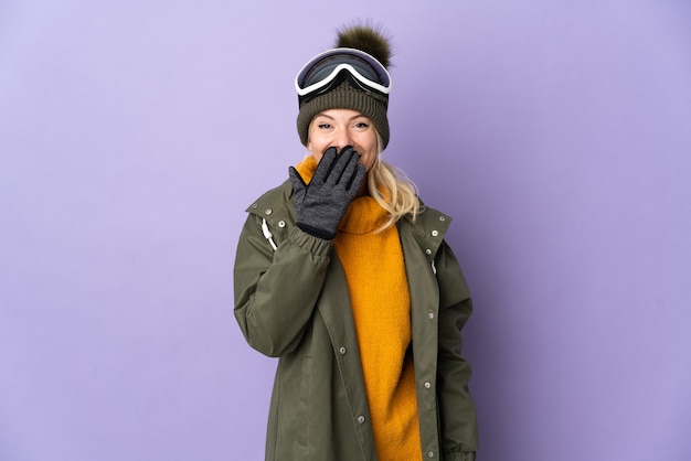 Skieur fille russe avec des lunettes de snowboard isolé sur mur violet heureux et souriant couvrant la bouche avec la main