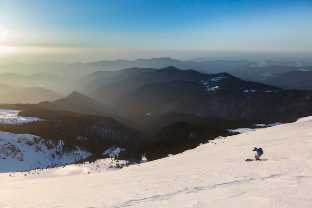 Un skieur freerider descend une large pente sur fond de chaînes de montagnes et de coucher de soleil