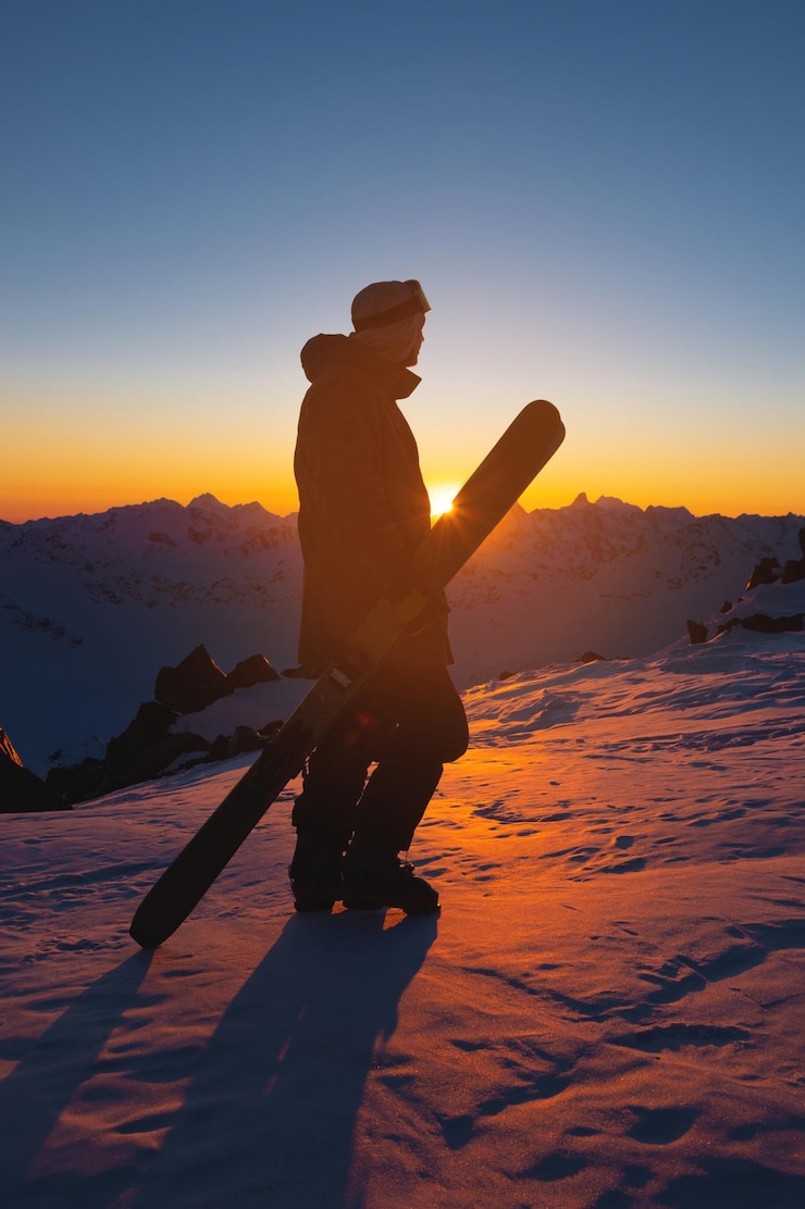 Photo un skieur se tient au sommet d'une colline enneigée dans une station de ski pendant un coucher de soleil d'hiver calme.