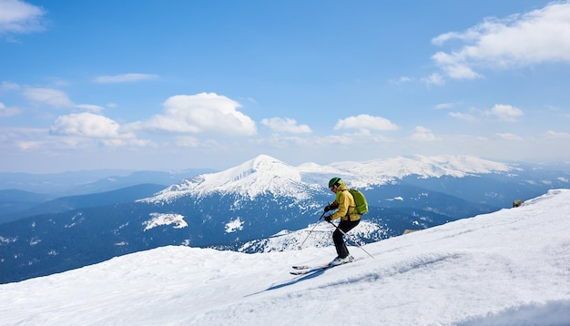 Skieur sportif en casque et lunettes de vêtements lumineux avec sac à dos descendant une pente enneigée raide