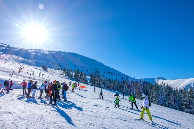 Skieurs adultes et enfants sur la piste de ski par une journée d'hiver ensoleillée