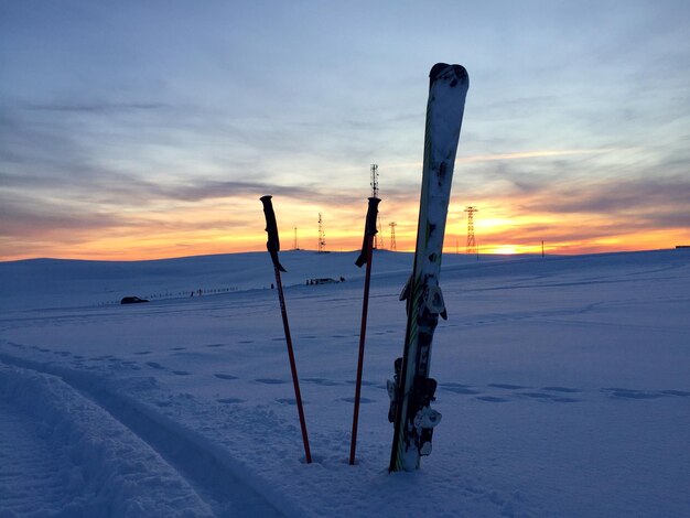 Des skis et des bâtons de ski dans la neige avec le coucher de soleil en arrière-plan