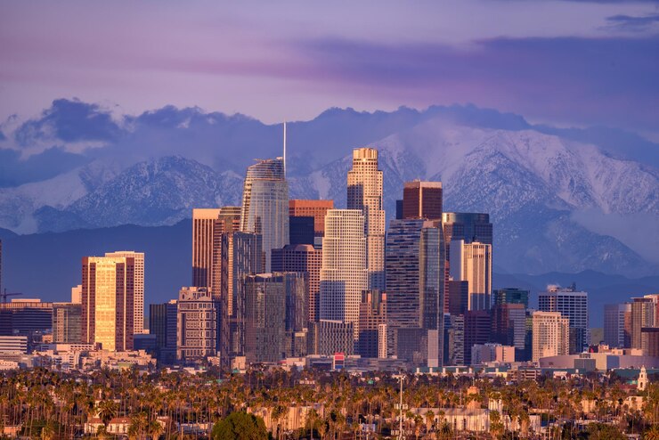 Photo skyline du centre-ville de los angeles avec des montagnes enneigées derrière au coucher du soleil