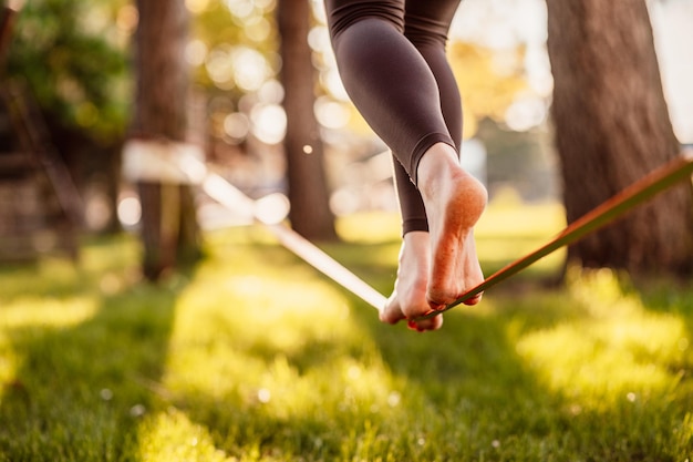 La slackline est une pratique en équilibre qui utilise généralement des sangles en nylon ou en polyester Fille marchant sur une slackline dans un parc pendant un coucher de soleil Slack line