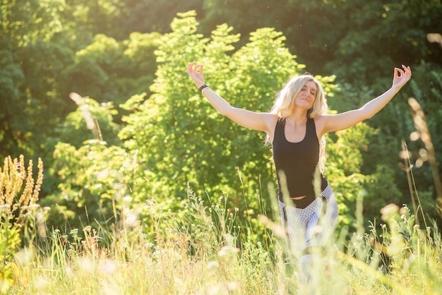 Slim femme pratique le yoga dans la nature par une journée ensoleillée