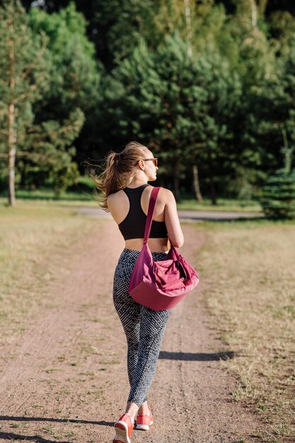 Slim fit femme marchant avec un gros sac de sport à l'extérieur dans le parc