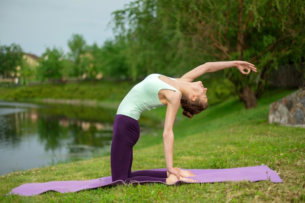 Slim jeune yogi brune effectue des exercices de yoga sur l'herbe verte