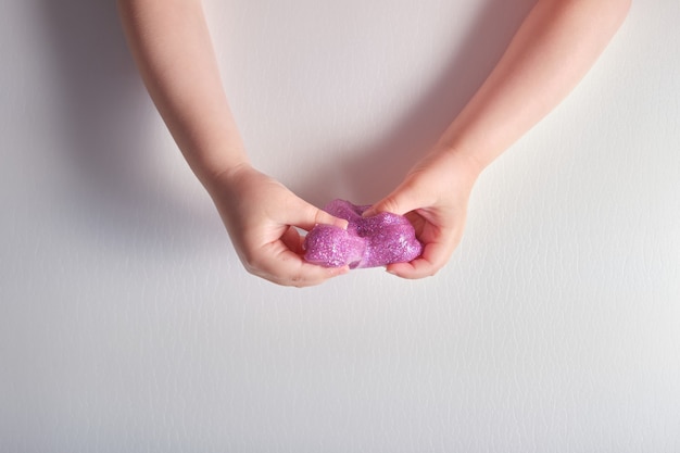 Slime rose brillant dans les mains des enfants sur une surface grise