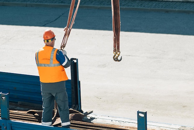 Slinger dans le casque et le gilet décharge les tuyaux et les raccords métalliques de la carrosserie du camion par temps clair Contexte de production Flux de travail authentique sur le chantier de construction Slinger au travail