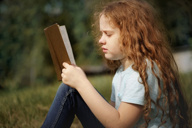 Smart petite fille lisant le livre à l&#39;extérieur.