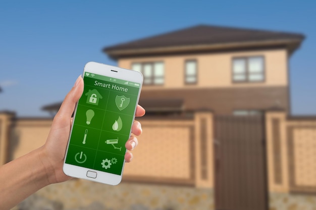 Smartphone avec application de sécurité à domicile dans une main sur le fond du bâtiment