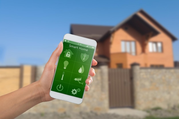 Smartphone avec application de sécurité à domicile dans une main sur le fond du bâtiment