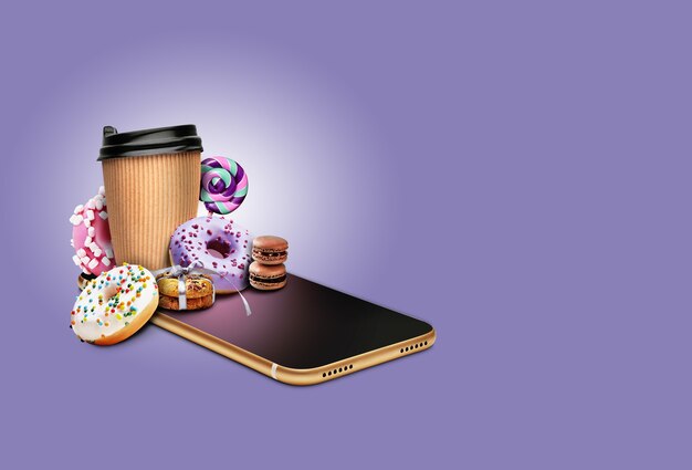 Smartphone avec beignets, cannes de bonbon, tasse de café en papier, biscuits attachés avec du ruban, macarons au chocolat dessus. Bonbons malsains.