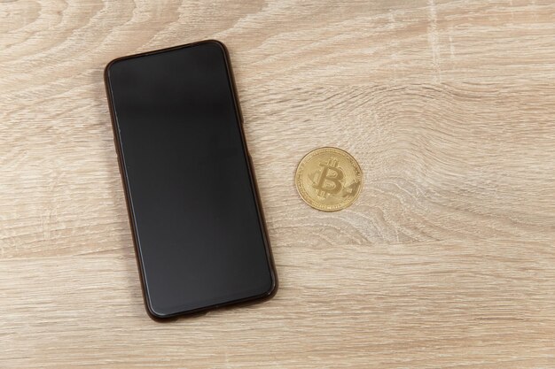 Photo un smartphone et des bitcoins en or sur une table en bois en gros plan