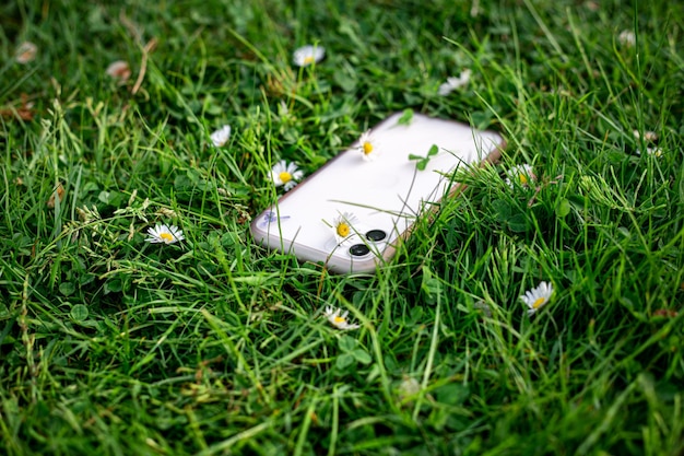 Smartphone blanc dans l'herbe verte parmi les marguerites