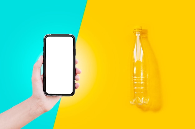 Smartphone avec blanc à l'écran dans la main masculine et bouteille en plastique transparente sur fond de couleurs jaune et cyan