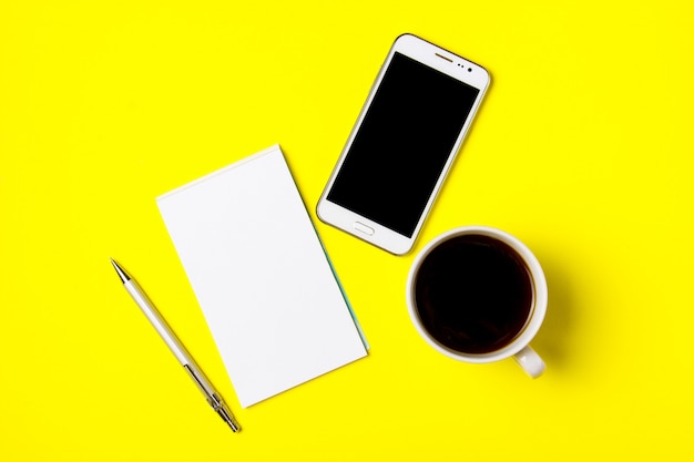 Smartphone, bloc-notes et tasse de café sur fond jaune