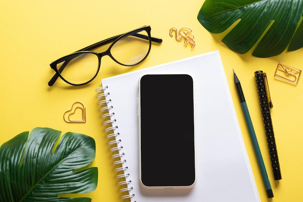 Smartphone bloc-notes vierge lunettes stylo trombones crayon sur fond jaune Bloguer sur le lieu de travail est une entreprise Espace de copie Vue de dessus à plat