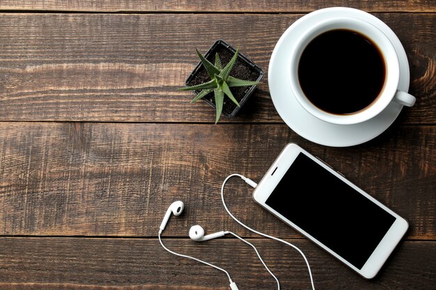 Smartphone avec casque et tasse de café sur une table en bois marron. vue d'en-haut