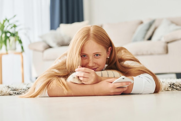 Avec smartphone dans les mains Une adolescente aux cheveux blonds est à la maison pendant la journée