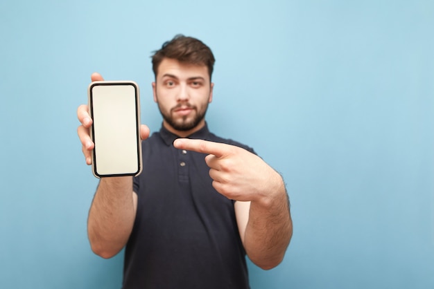 Smartphone avec un écran blanc vierge dans les mains d'un homme adulte avec une barbe, portant une chemise sombre