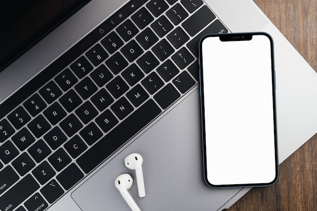 Smartphone à écran blanc vierge sur fond de bois avec un ordinateur à côté. Clé chroma.