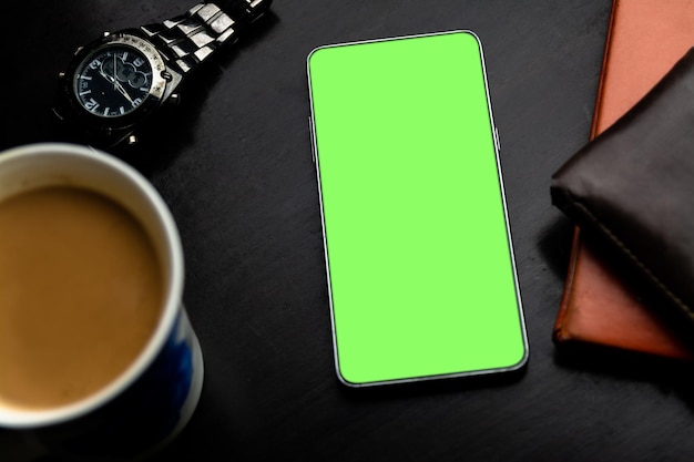 Un smartphone à écran vert sur le bureau avec une tasse de café et une montre de poignet