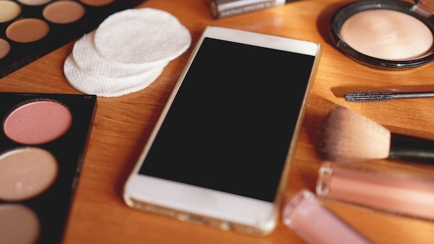 Smartphone avec écran vide et cosmétiques sur fond en bois clair. Vue de dessus, mise à plat. Maquette de téléphone portable.