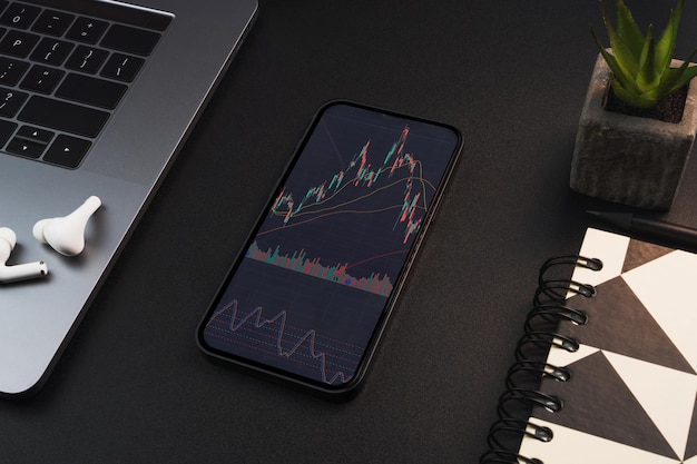 Smartphone avec graphique boursier financier sur l'écran sur fond noir tableau Environnement de bureau Bourse