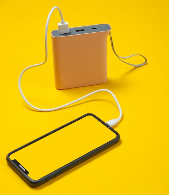 Smartphone moderne en charge avec power bank sur jaune.