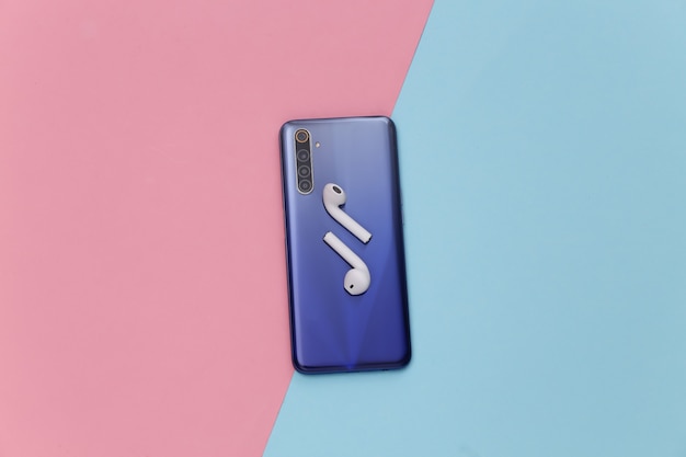 Smartphone moderne avec écouteurs sans fil sur fond pastel rose bleu.