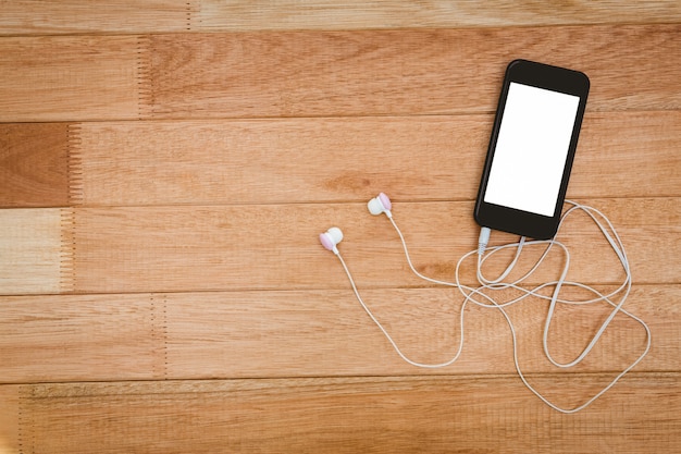 Smartphone noir avec un casque blanc sur le bureau en bois