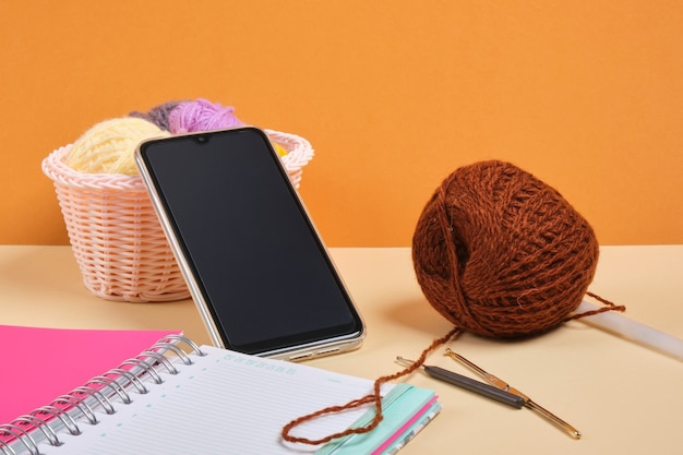 smartphone, ordinateur portable et crochets et fils à tricoter dans un panier, formation au tricot en ligne