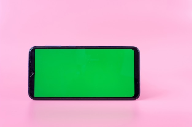 Smartphone en position horizontale avec un écran vert sur fond rose, incrustation de chrominance, maquette.