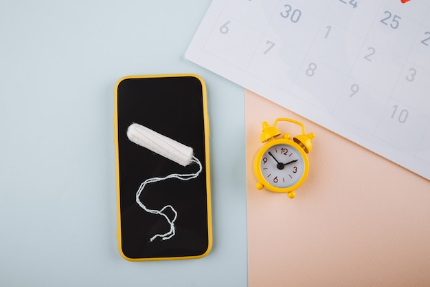 Smartphone pour suivre votre cycle menstruel et pour les marques. PMS et le concept des jours critiques. Tampon en coton, tampon quotidien et alarme jaune sur fond bleu rose.