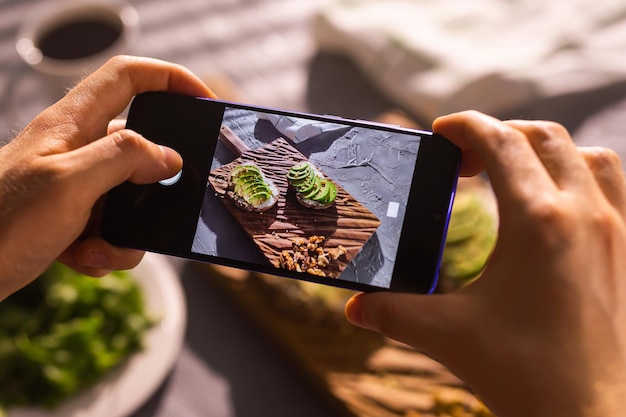 Smartphone prenant une photo à partir de sandwichs sains bio avec main d'homme à l'avocat