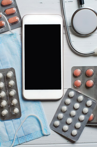 Smartphone, stéthoscope et médicaments sur fond blanc