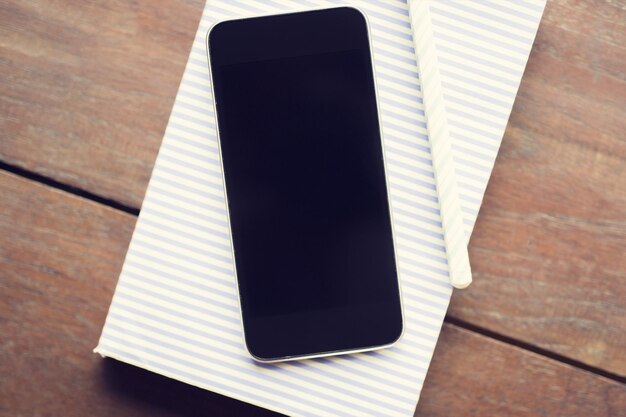 Un smartphone vide avec un journal et un stylo clairs sur une maquette de table en bois