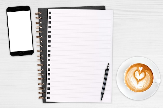 Un smartphone vierge ouvert avec un stylo et une tasse de café au lait sur une table en bois