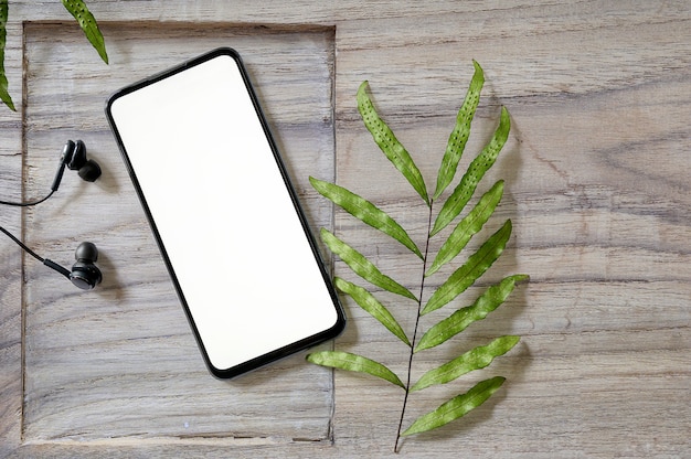 Photo smartphone vue de dessus avec écran blanc et écouteurs sur fond en bois.