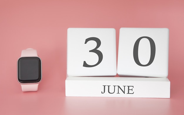 Smartwatch avec calendrier cube et date 30 juin sur table rose.