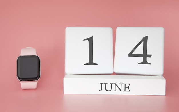 Smartwatch avec calendrier cube et date du 14 juin sur table rose.